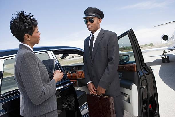Mid-adult businesswoman and mid-adult chauffeur standing in front of limousine and talking.